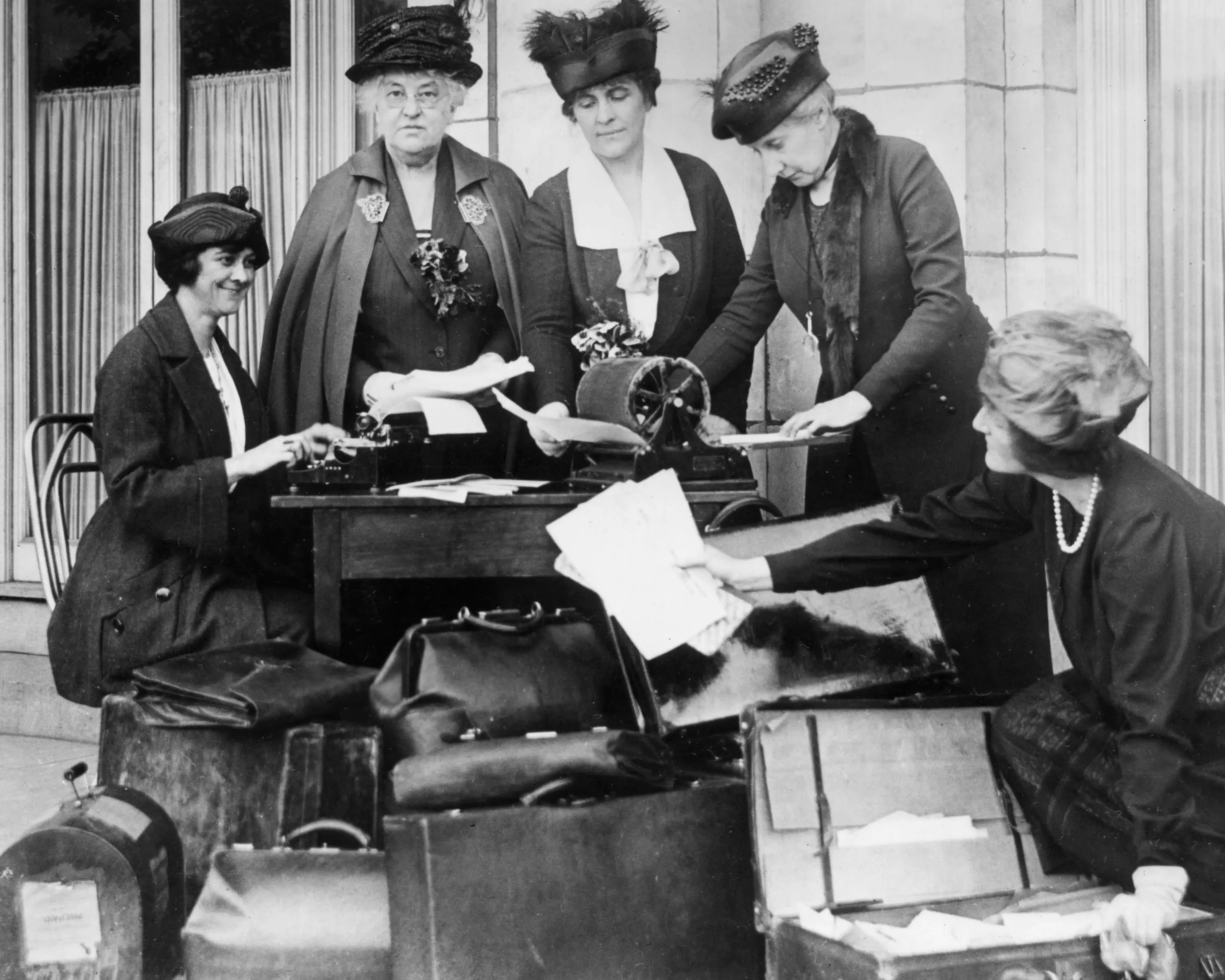 League of Women Voters representatives gather around a table on a sidewalk while writing and mimeographing news releases to hand out at train stops en route to the Democratic Convention.