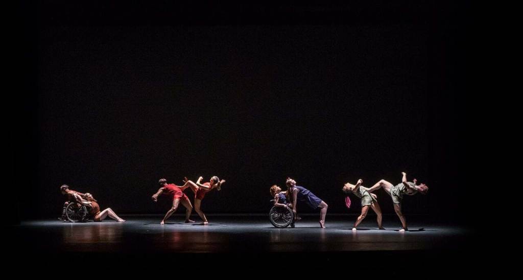 From Dancing Wheels Company & School: Four pairs of dancers in a beam of light; two dancers are wheelchair users.