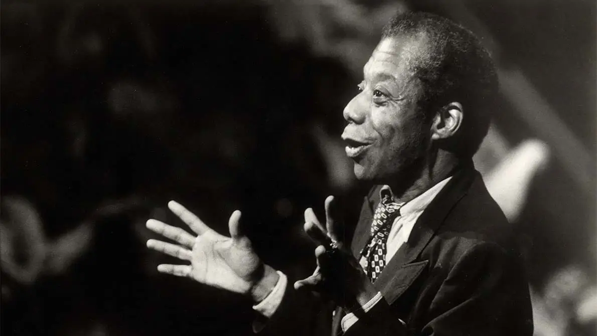 A black and white photo of James Baldwin speaking to a crowd. 